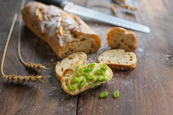 Μισό φέτες μπαγκέτα ή γαλλικό ψωμί ολοκληρώνεται με πράσινο κρεμμύδι άνοιξη σε ένα ρουστίκ ξύλινο τραπέζι, αντίγραφο χώρου — Φωτογραφία Αρχείου