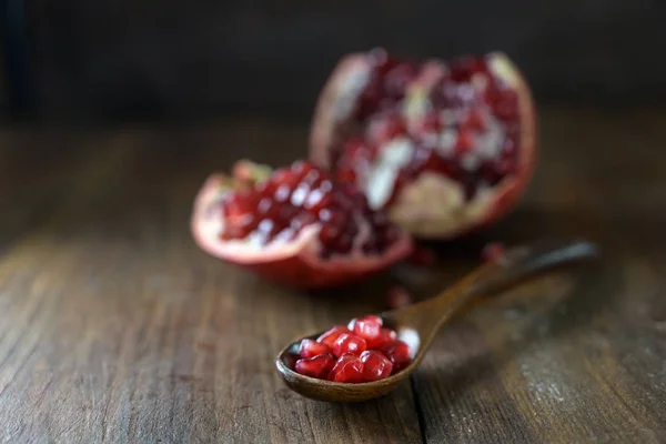 Granatäpple frön på en sked och frukten suddig i bakgrunden, mörk rustik träbord med kopieringsutrymme — Stockfoto