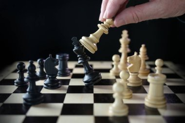 İnsan eli satranç oynuyor ve kralı yeniyor. Satranç tahtasında siyah bir arka plana karşı şah mat.