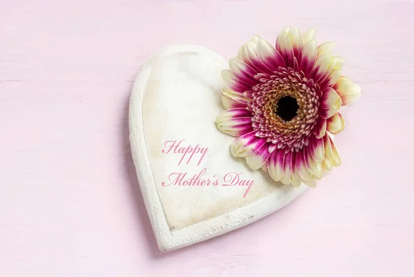 Wit geschilderd houten hart vorm en een bloem hoofd op een fel roze achtergrond, tekst Happy Mother 's Day, bovenaanzicht van boven met kopieerruimte — Stockfoto