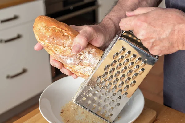 Человек теряет твёрдый хлеб на терке, чтобы получить хлебные крошки — стоковое фото