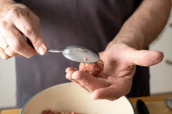 Hands of a man are forming balls of raw minced meat and other ingredients with a spoon to make meatballs — Stok fotoğraf