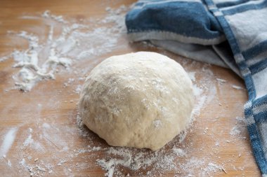 Ekmek ya da pasta için hamur mayası ahşap bir pişirme tahtasına yükselmeye hazır biraz un ve mavi bir mutfak havlusu, seçilmiş odak noktası, dar bir tarla derinliği