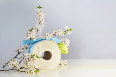 Hicivsel hediye, Paskalya yumurtalı tuvalet kağıdı, kurdele ve kiraz çiçeği dalları, gıpta edilen ürünler, covid-19 salgını, koronavirüs salgını, fotokopi alanı olan açık gri arka plan, seçik alan derinliği, seçilmiş alan derinliği