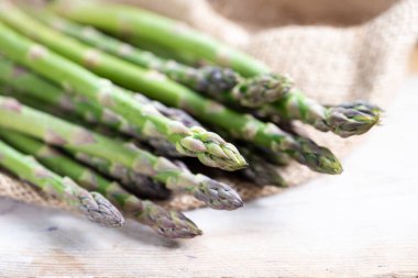 Çuval bezi ve hafif kırsal ahşap üzerinde organik yeşil kuşkonmaz (asparagus officinalis), seçilmiş odak ve çok dar alan derinliği ile yakın çekim