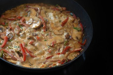 Siyah bir sobada biber, mantar ve soğanlı kremalı sebze yahnisi, kopyalama alanı, seçilmiş odak, dar alan derinliği.