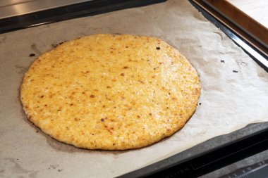 Fırın tepsisindeki parçalanmış karnabahar ve peynirden taze pişmiş pizza kabuğu, düşük karbonhidratlı veya ketojenik diyetle zayıflamak için sağlıklı bir tarif, seçilmiş odak, dar bir alan derinliği.
