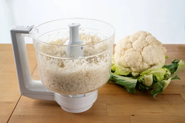 cauliflower shredded in a food processor for healthy low carb pizza crust or as vegetable rice replacement on a wooden kitchen table, selected focus, narrow depth of field