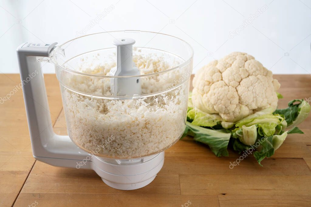 cauliflower shredded in a food processor for healthy low carb pizza crust or as vegetable rice replacement on a wooden kitchen table, selected focus, narrow depth of field