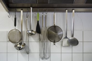Elemeler, omurgalar, çırpılar ve diğer aletler bir kantin mutfağındaki fayanslı kaputta asılı, seçilmiş odak noktası