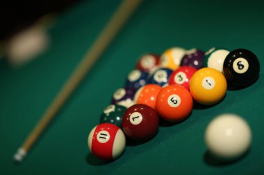 Yeşil kumaş üzerinde bilardo oyunu. Çok renkli bilardo topları sayılar, işaret ve bilardo masasının üzerinde üçgen şeklinde üçgen şeklinde. Bilardo ve bilardo topları yakın mesafede..