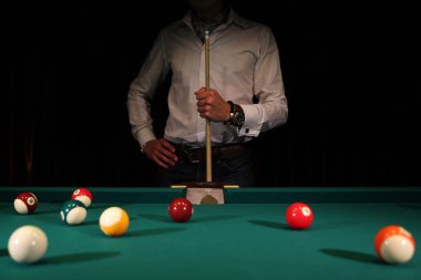 Yeşil kumaş üzerinde bilardo oyunu. Elinde ıstakayla bir erkek oyuncu. Bilardo masasında numaralar olan bilardo topları. Aktif eğlence ve eğlence. Bilardo ve bilardo topları.