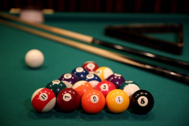 Yeşil kumaş üzerinde bilardo oyunu. Sayılar, iki ipucu, bir bilardo topu ve bir bilardo masasının üzerinde üçgen şeklinde çok renkli bilardo topları. Bilardo topları yakın mesafede..