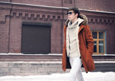 Şehirde tuğla üzerinde yürüyen bir ceket giyen moda adam duvar bac
