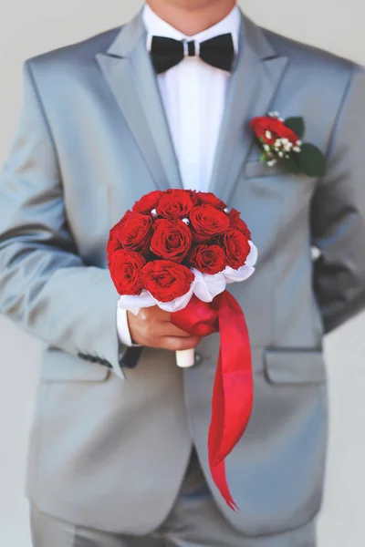 Handsome groom holding wedding bouquet of red roses flowers in s — Stock Photo, Image