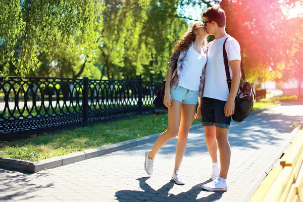 Молодая пара влюбленных целуется гуляя в городском парке на летнем солнце — стоковое фото