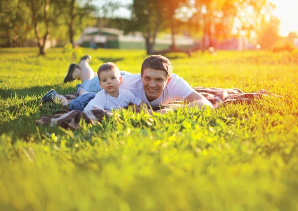 Soleado retrato feliz padre con hijo hijo acostado en el verde gr — Foto de Stock