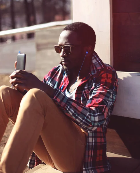 Retrato de moda jovem homem africano ouve música usando smartp — Fotografia de Stock