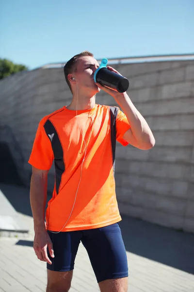 Sport, fitness - young runner man drinks from a bottle the water — Stock Photo, Image