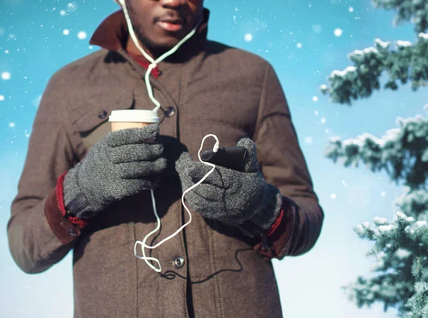 Africano hombre escucha música, el uso de teléfono inteligente celebración de café cu — Foto de Stock
