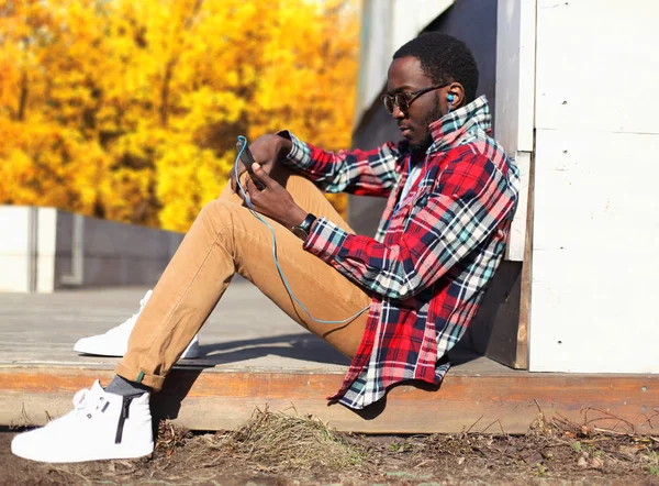 Moda joven africano hombre usando teléfono inteligente se sienta en el otoño pa — Foto de Stock