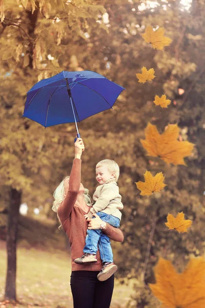 Gelukkig moeder met haar kind houdt een paraplu in een herfst park — Stockfoto