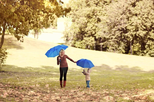 Matka a dítě chodí s deštníky v podzimním parku, yello — Stock fotografie