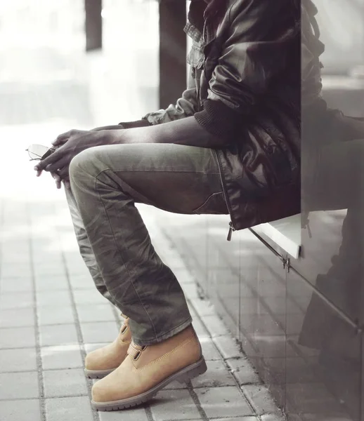 Moda uomo africano in giacca nera, jeans e stivali seduto in — Foto Stock