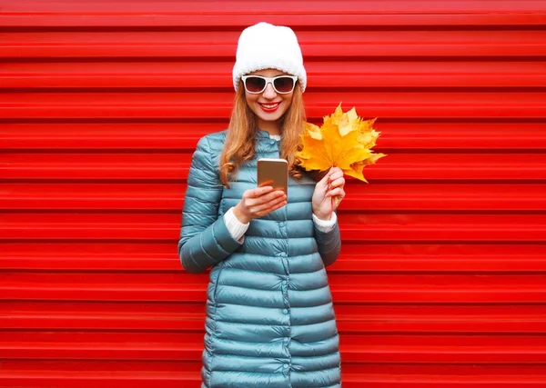 Moda otoño sonriente mujer usando smartphone sostiene arce amarillo —  Fotos de Stock