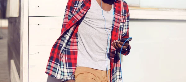 Fashion man listens to music on a smartphone in plaid red shirt — Stock Photo, Image