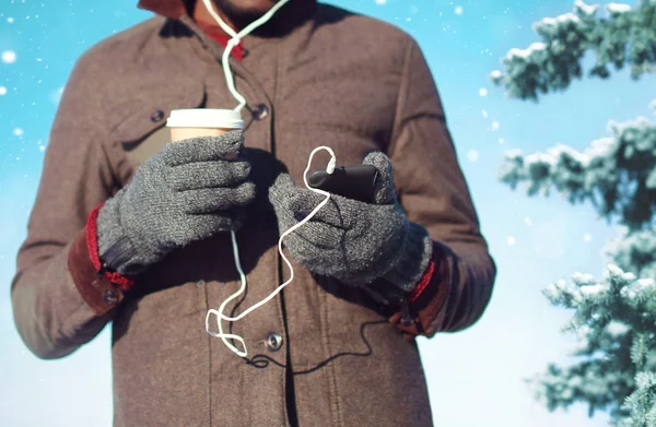 Man listens to music on a smartphone holds coffee cup in hand on