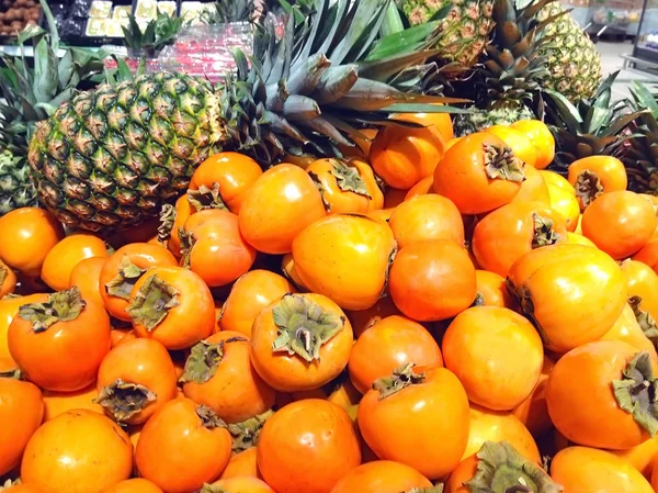 Muchas frutas caqui y piñas que yacen en el supermercado —  Fotos de Stock
