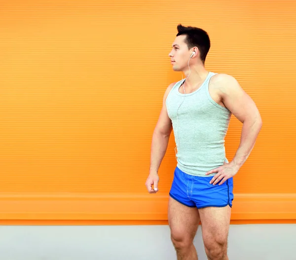 Sportsman listens to music on a colorful orange background. Fitn — Stock Photo, Image