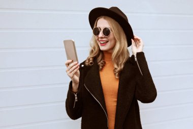 Şık bir şekilde gülümseyen genç kadın akıllı telefonla selfie çekiyor. 