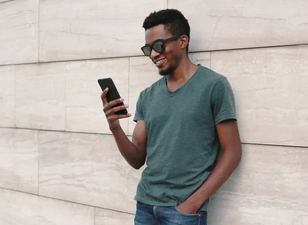 Retrato sonriente hombre africano con teléfono vistiendo camiseta, sunglas —  Fotos de Stock