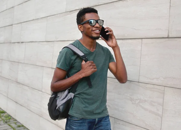 Joven estudiante africano sonriente llamando en el teléfono inteligente usando —  Fotos de Stock