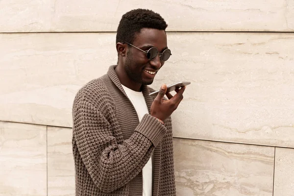 Szczęśliwy uśmiechnięty Afrykanin człowiek ze smartfonem za pomocą polecenia głosowego re — Zdjęcie stockowe