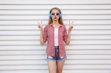 Kulaklıklı çekici genç bir kadın müzik dinliyor kırmızı dudaklar üflüyor beyaz arka planda tatlı bir öpücük yolluyor.