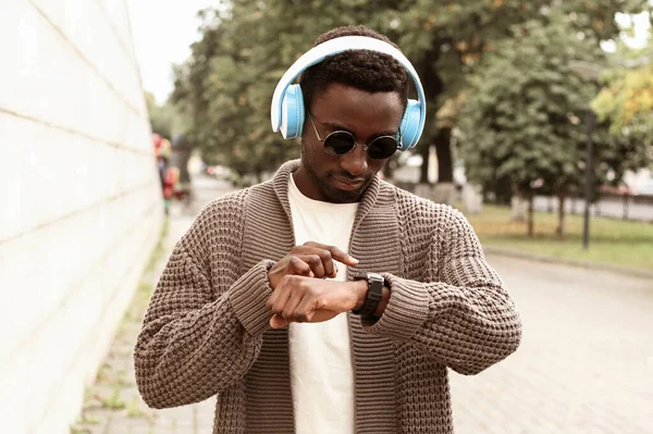 肖像アフリカの男を見てスマートウォッチで音声アシスタントを使用するか 市内通りのワイヤレスヘッドフォンで呼び出します — ストック写真
