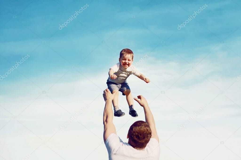 Happy father throwing his son child into the air, carefree having fun outdoors over the blue sky background, family and father's day - concept