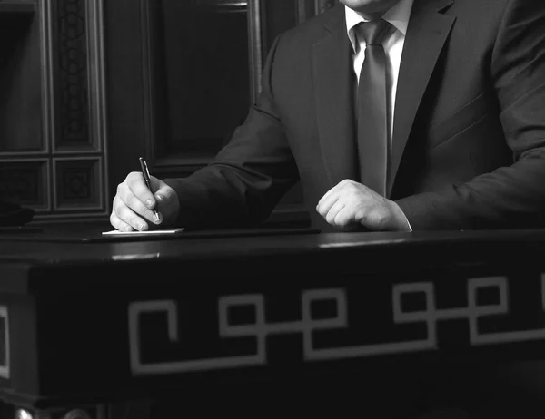 Närbild av affärsmannen sitter vid bord och underteckna dokument, svartvit foto — Stockfoto