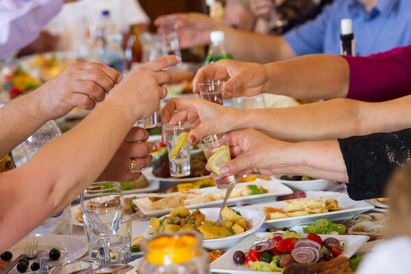 closeup photo of hands clinking glasses with vodka at party