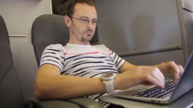 Orta yaşlı adam onun iş seyahati sırasında uçak kabin içinde laptop üzerinde kayıtsızca giyinmiş