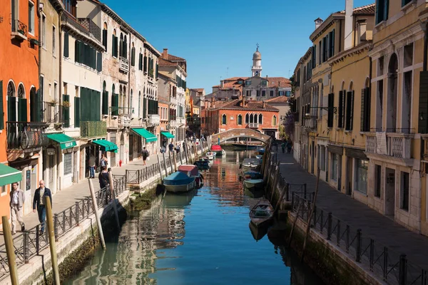 VENECIA, ITALIA - 09.04.2017: Calle estrecha con un canal, puente, barcos y turistas en Venecia — Foto de Stock