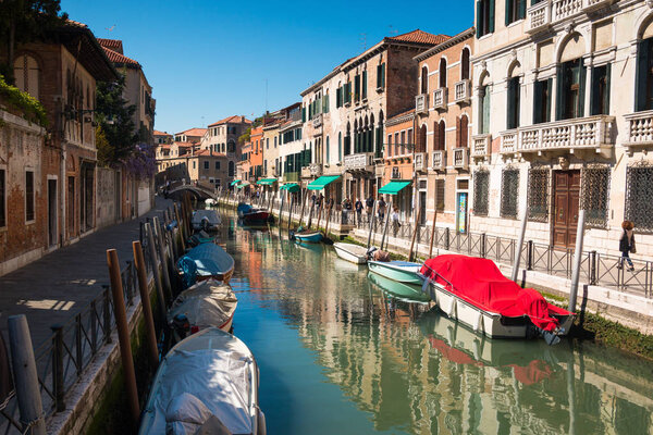VENICE, ITALY - 09.04.2017: Narrow street with a canal, bridge, boats and tourists in Venice