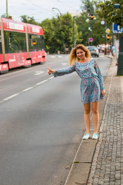 젊은 여자는 시의 거리에서 히 치 하이킹을 하 고 — 스톡 사진