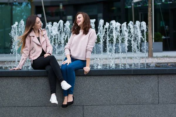 Две красивые молодые женщины веселятся рядом с фонтаном на улице города — стоковое фото