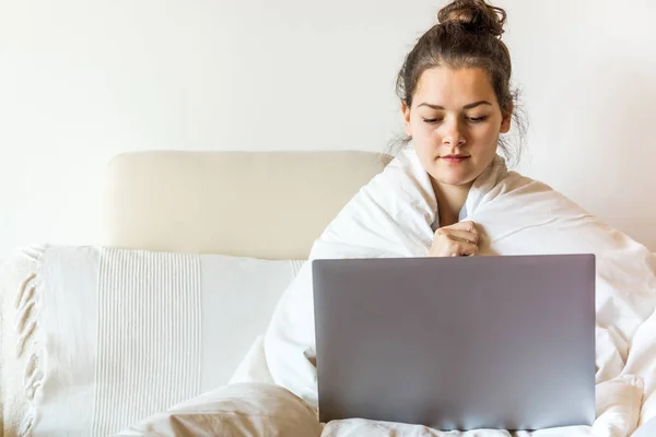 Mooie jonge vrouw vallende deken zit op bed met laptop — Stockfoto