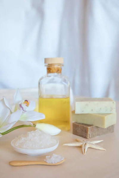 Ambiente de bienestar. Sal marina, jabón, toalla, aceite y flores sobre fondo de madera — Foto de Stock