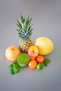 Gri arka planda farklı tropikal meyveler ve yeşil smoothie, sağlıklı beslenme tarzı konsepti